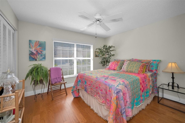 bedroom with a textured ceiling, wood finished floors, a closet, baseboards, and ceiling fan