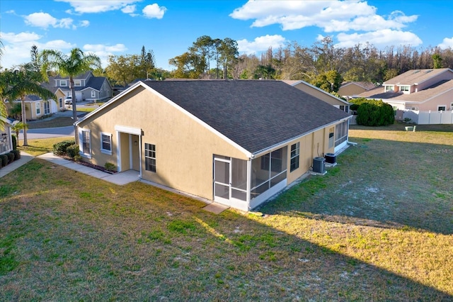 back of house with central air condition unit, roof with shingles, a yard, and a sunroom