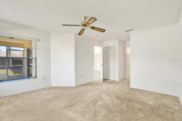 carpeted spare room with a ceiling fan, visible vents, and a textured ceiling