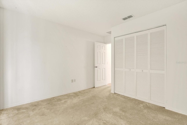 unfurnished bedroom featuring light colored carpet, visible vents, and a closet