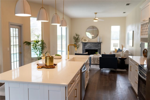 kitchen with a sink, a high end fireplace, white cabinets, dark wood-style floors, and an island with sink