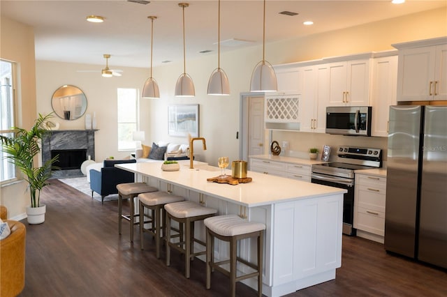 kitchen with dark wood-style flooring, stainless steel appliances, a premium fireplace, open floor plan, and a kitchen bar