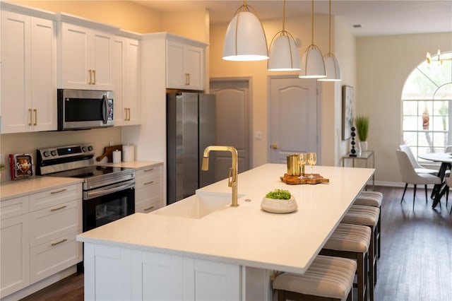 kitchen with a center island with sink, white cabinets, appliances with stainless steel finishes, dark wood-type flooring, and a sink