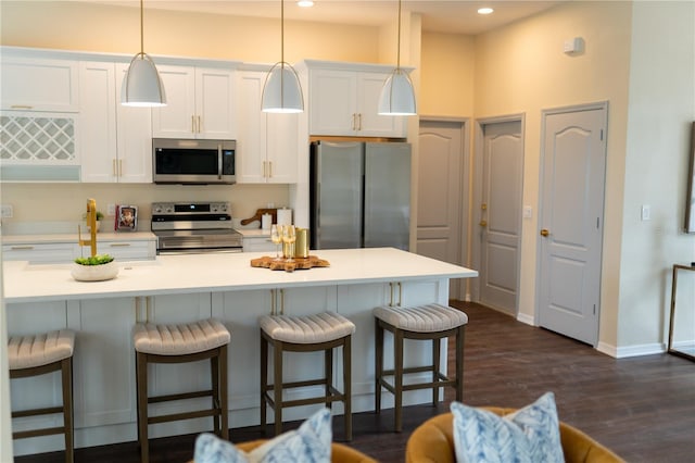 kitchen with dark wood-style flooring, light countertops, appliances with stainless steel finishes, white cabinetry, and a kitchen breakfast bar