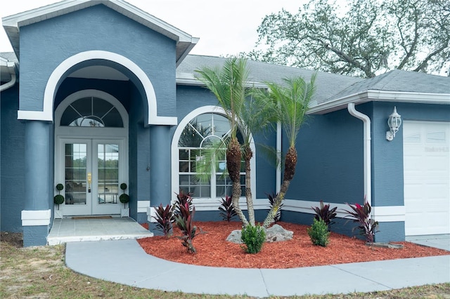 doorway to property with a garage, french doors, and stucco siding