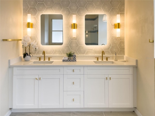 bathroom featuring a shower, double vanity, a sink, and baseboards