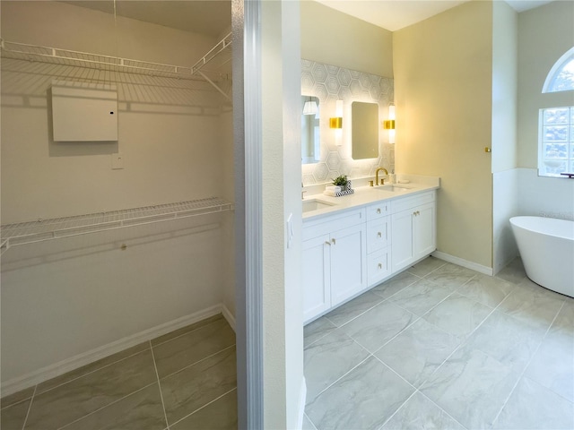 full bathroom with double vanity, baseboards, a spacious closet, a freestanding tub, and a sink