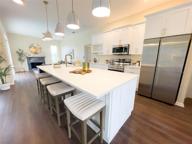 kitchen with dark wood-style flooring, light countertops, appliances with stainless steel finishes, a kitchen island with sink, and white cabinetry