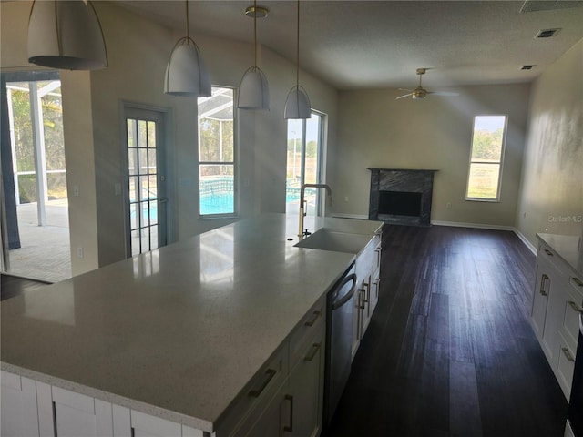 kitchen with a kitchen island with sink, dark wood-type flooring, a fireplace, a sink, and white cabinets