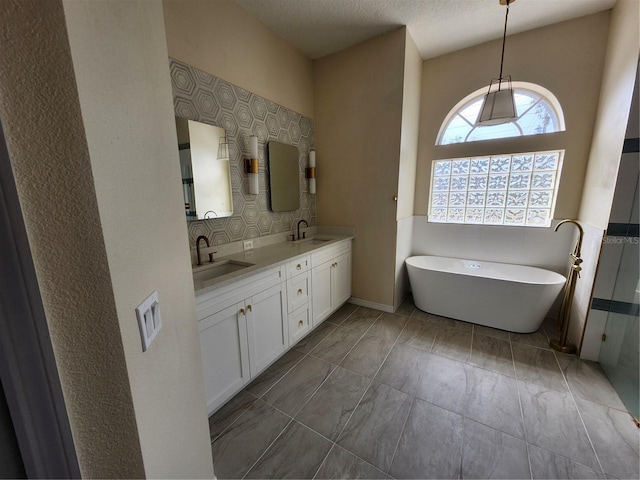 bathroom with a textured ceiling, double vanity, a freestanding tub, and a sink