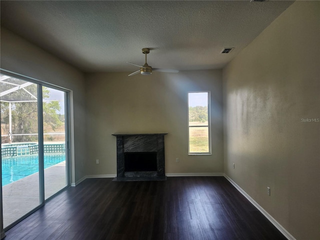 unfurnished living room with a fireplace, dark wood finished floors, ceiling fan, a textured ceiling, and baseboards