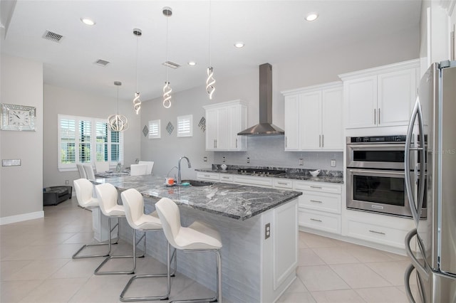 kitchen with a sink, visible vents, wall chimney range hood, appliances with stainless steel finishes, and backsplash