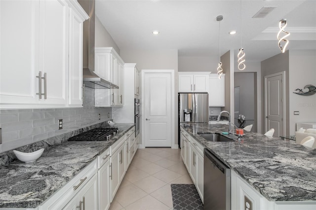 kitchen featuring visible vents, white cabinets, stainless steel appliances, wall chimney range hood, and a sink