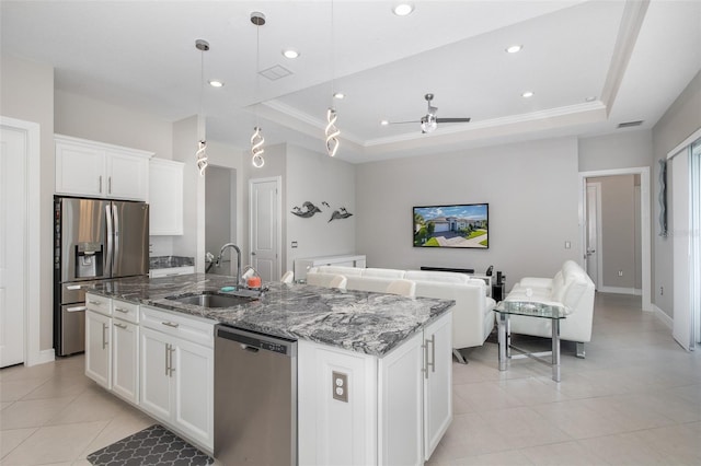 kitchen featuring stone countertops, a raised ceiling, appliances with stainless steel finishes, a kitchen island with sink, and a sink