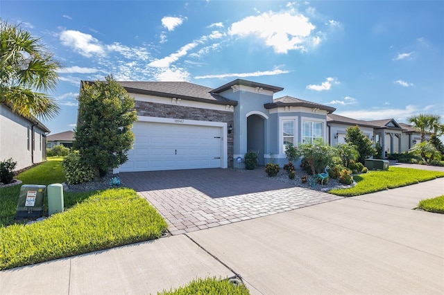 view of front facade with an attached garage, stone siding, decorative driveway, stucco siding, and a front yard