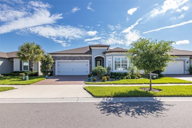 view of front of property featuring a front yard, decorative driveway, an attached garage, and stucco siding