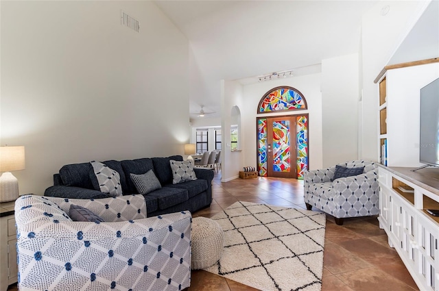 living room with visible vents, track lighting, tile patterned floors, a towering ceiling, and arched walkways