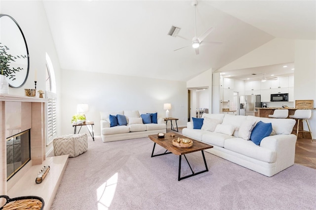 carpeted living room with visible vents, high vaulted ceiling, a ceiling fan, a premium fireplace, and baseboards