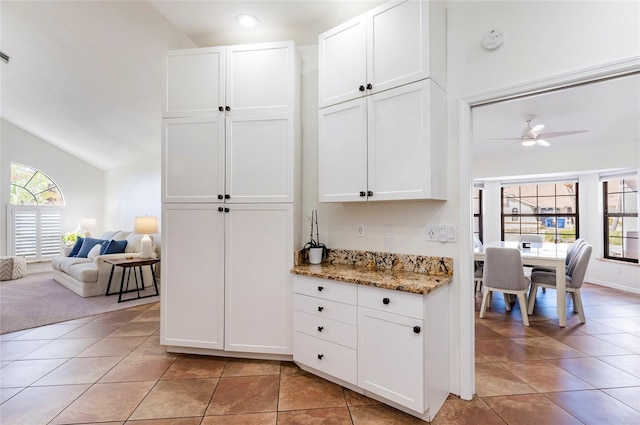 kitchen featuring white cabinets, light tile patterned floors, light stone countertops, ceiling fan, and vaulted ceiling