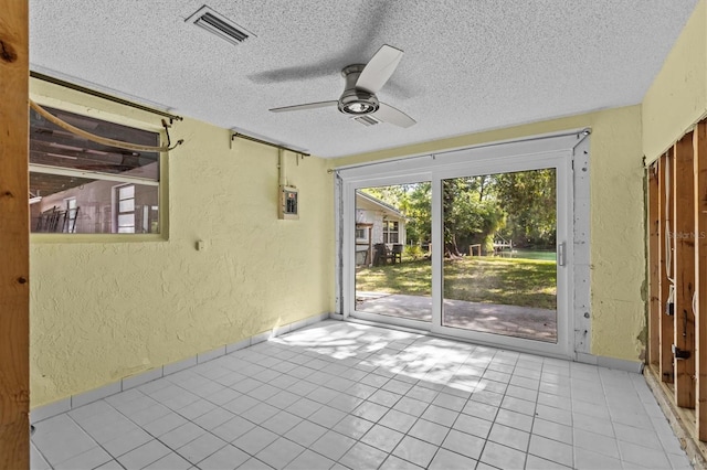 tiled spare room featuring a ceiling fan, a textured wall, visible vents, and a textured ceiling