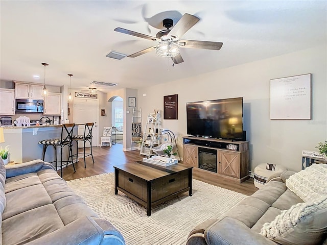 living area featuring visible vents, light wood-style floors, arched walkways, and ceiling fan