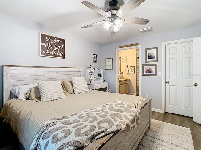 bedroom with a ceiling fan, wood finished floors, visible vents, baseboards, and ensuite bath