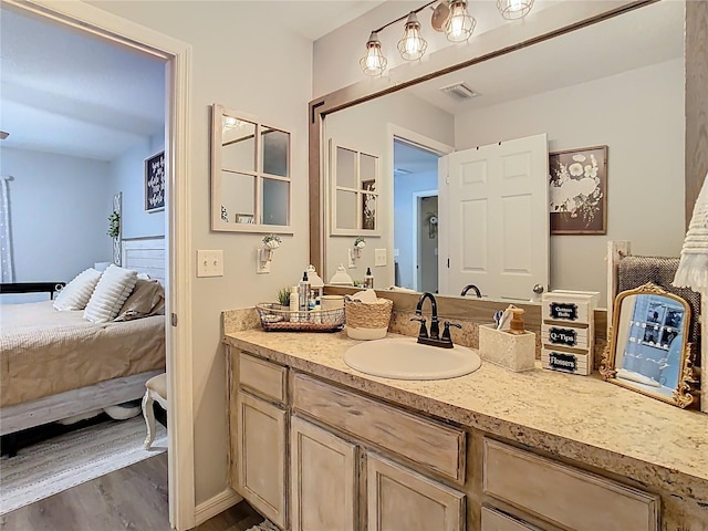 ensuite bathroom featuring vanity, wood finished floors, visible vents, baseboards, and ensuite bath