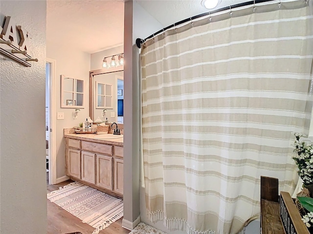 bathroom featuring curtained shower, baseboards, wood finished floors, a textured wall, and vanity