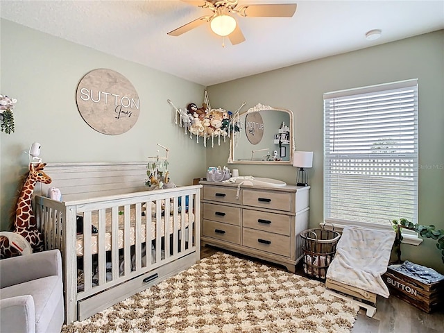 bedroom with a crib, ceiling fan, and wood finished floors