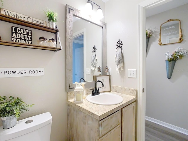 half bath featuring baseboards, toilet, wood finished floors, and vanity