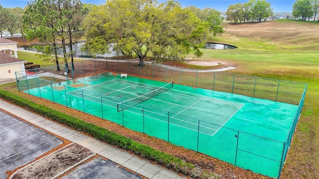 view of tennis court with a yard, a water view, and fence