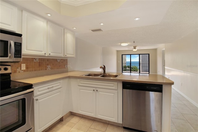 kitchen featuring visible vents, a wainscoted wall, a sink, appliances with stainless steel finishes, and a peninsula