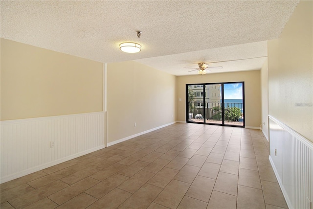 spare room with a ceiling fan, a wainscoted wall, and a textured ceiling