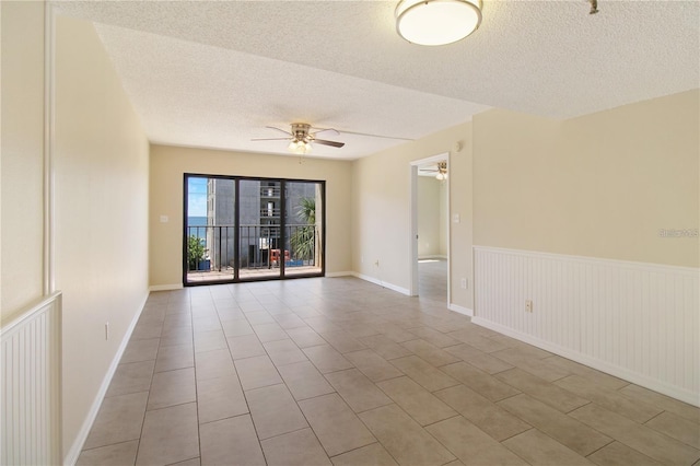 tiled empty room featuring a wainscoted wall, a textured ceiling, and ceiling fan