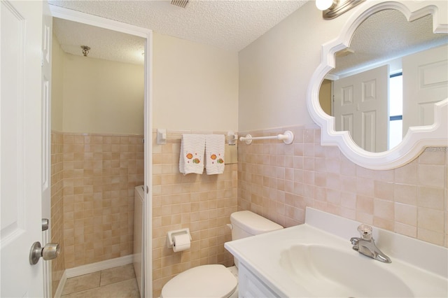 bathroom with vanity, a textured ceiling, tile patterned floors, toilet, and tile walls