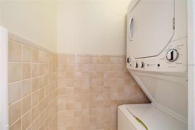 washroom featuring laundry area, tile walls, a wainscoted wall, and stacked washing maching and dryer