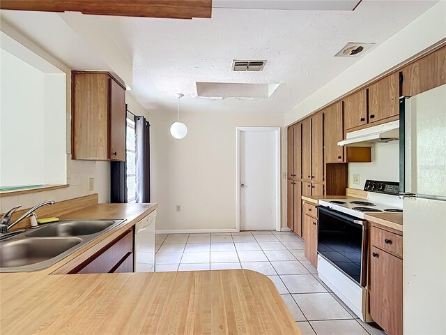 kitchen featuring white appliances, light tile patterned floors, visible vents, a sink, and under cabinet range hood