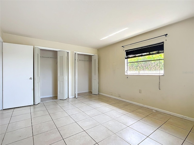 unfurnished bedroom with light tile patterned floors, baseboards, and multiple closets