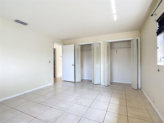 unfurnished bedroom featuring light tile patterned floors, visible vents, baseboards, and multiple closets