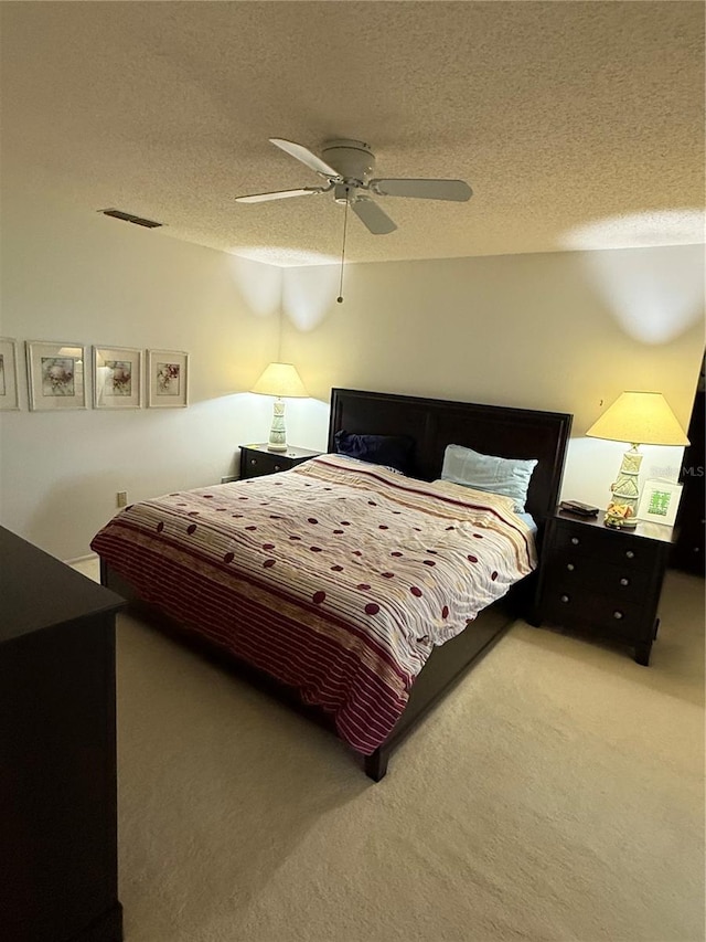 bedroom featuring visible vents, carpet floors, a textured ceiling, and a ceiling fan