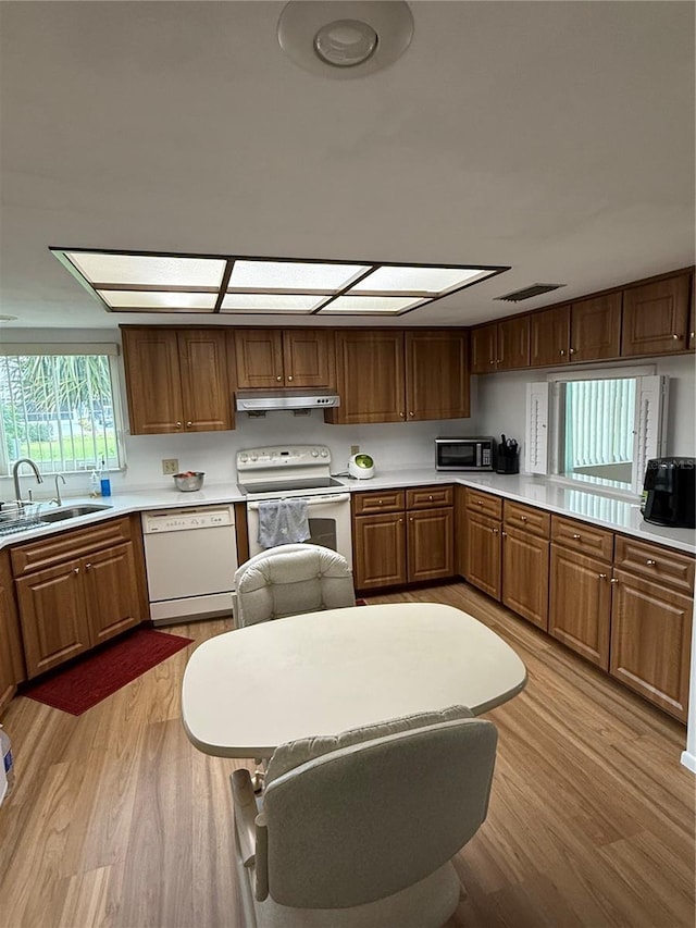 kitchen with white appliances, a sink, light countertops, light wood-style floors, and under cabinet range hood