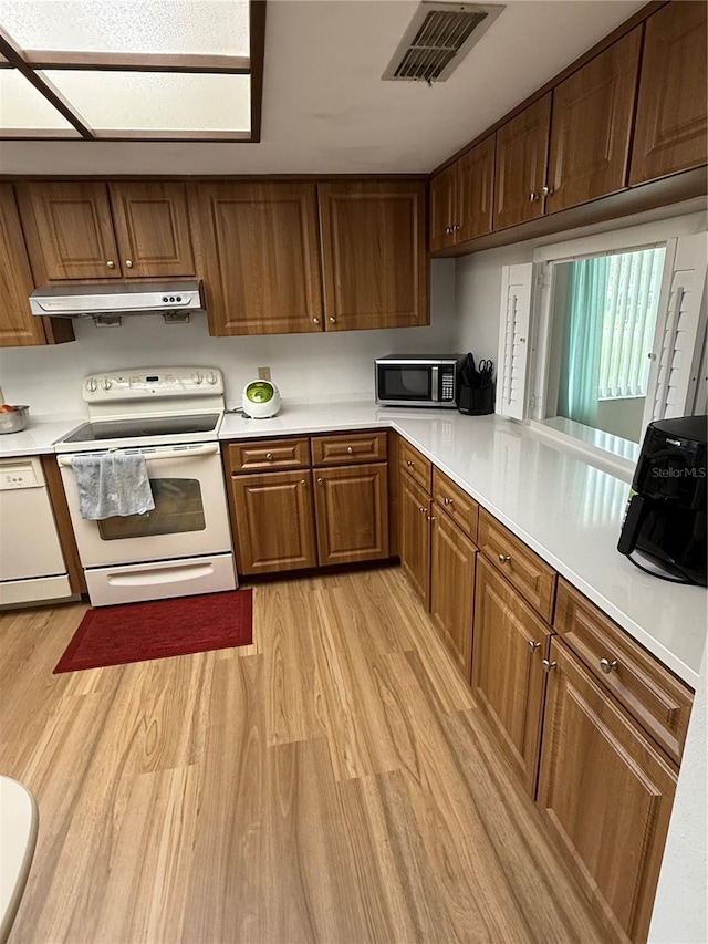 kitchen featuring under cabinet range hood, visible vents, white appliances, and light wood-style floors