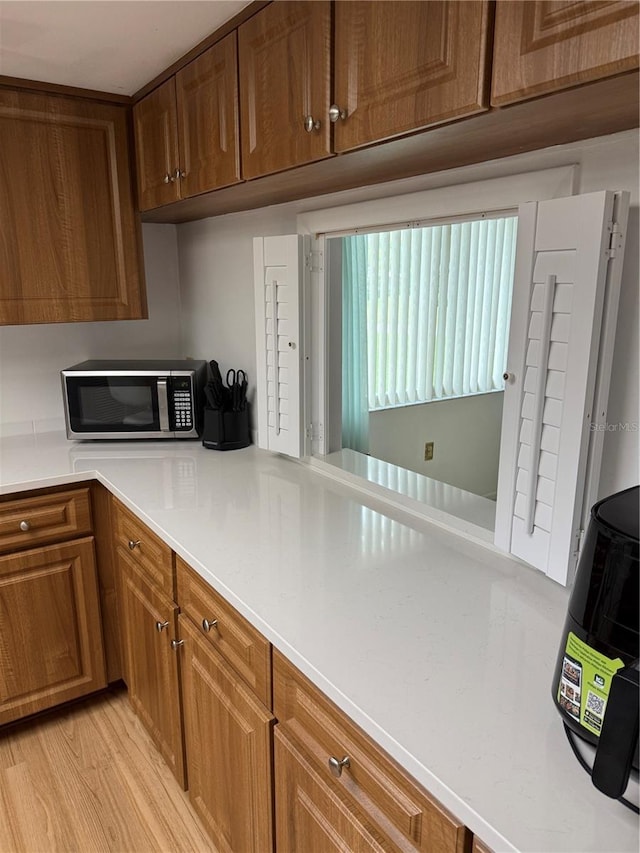 kitchen with light wood finished floors, stainless steel microwave, brown cabinets, and light countertops