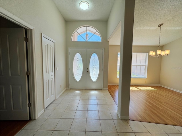 entrance foyer featuring a chandelier, baseboards, a textured ceiling, and light tile patterned flooring