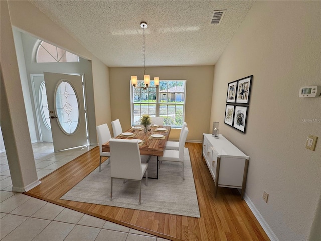 dining space featuring a notable chandelier, visible vents, a textured ceiling, and light wood-style floors