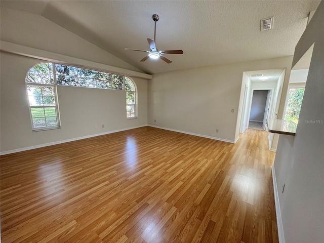 spare room featuring light wood finished floors, visible vents, a textured ceiling, and vaulted ceiling