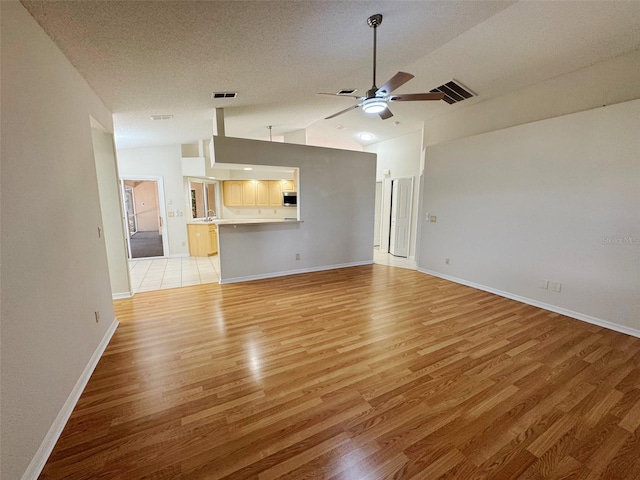 unfurnished living room featuring visible vents, light wood-style flooring, a textured ceiling, and lofted ceiling