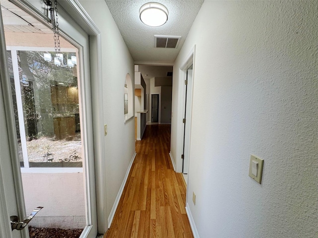 corridor featuring light wood-type flooring, visible vents, a textured ceiling, baseboards, and a chandelier