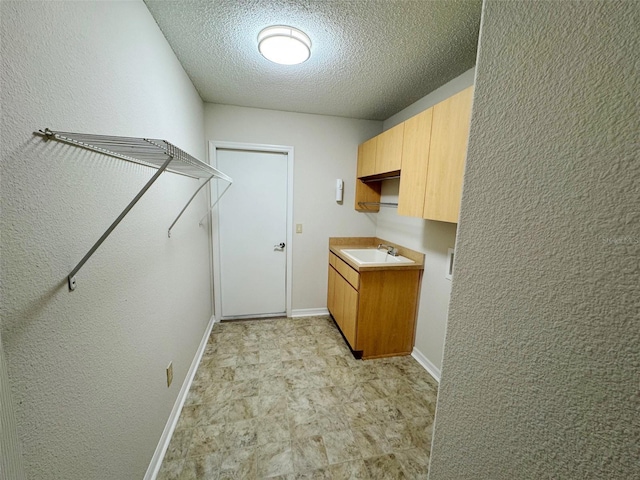 washroom featuring a textured ceiling, a textured wall, baseboards, and a sink