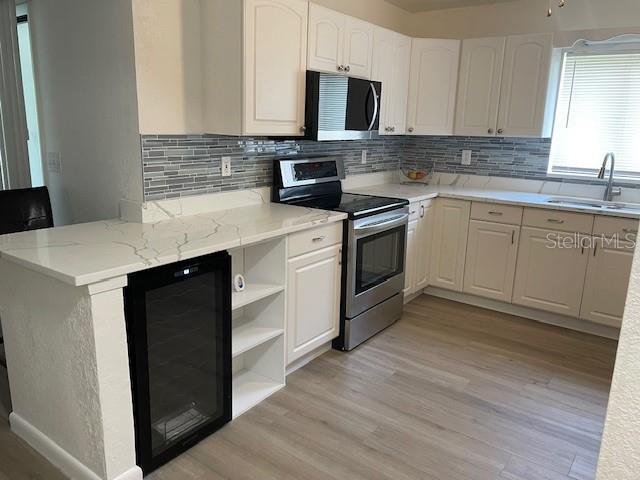 kitchen featuring a sink, stainless steel appliances, beverage cooler, and light wood-style flooring